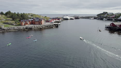 Scenic-shot-of-stand-up-paddlers-and-a-small-boat-going-in-towards-Hamnoy-Harbor-on-Lofoten-Island