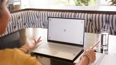 using laptop with blank screen, indian woman gesturing while holding pencil at table, copy space