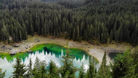 dron de 4k volando a través de los árboles para revelar un hermoso lago azul con reflejo de nubes y luego inclinarse hacia arriba para mostrar hermosas montañas en dolomitas en italia