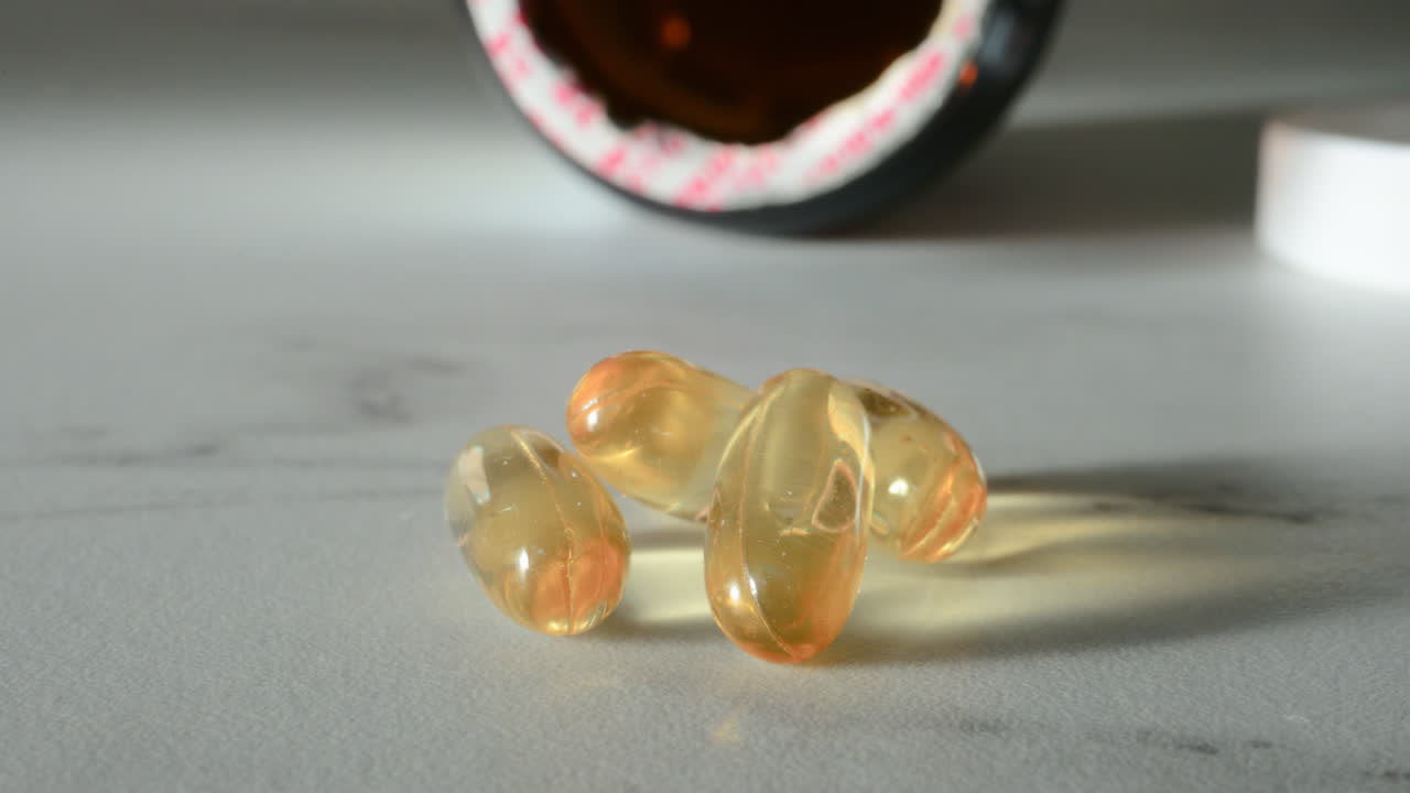 Close up of fish oil supplements scattered on a white table near a pill bottle