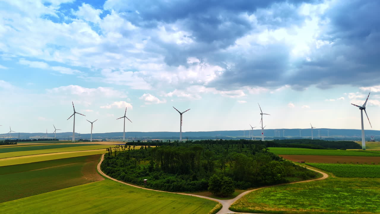 Wind mills rotate producing green energy. Summer day footage over the field on a gloomy day