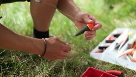 male angler prepares float bobber for fishing and pulls the fishing line through