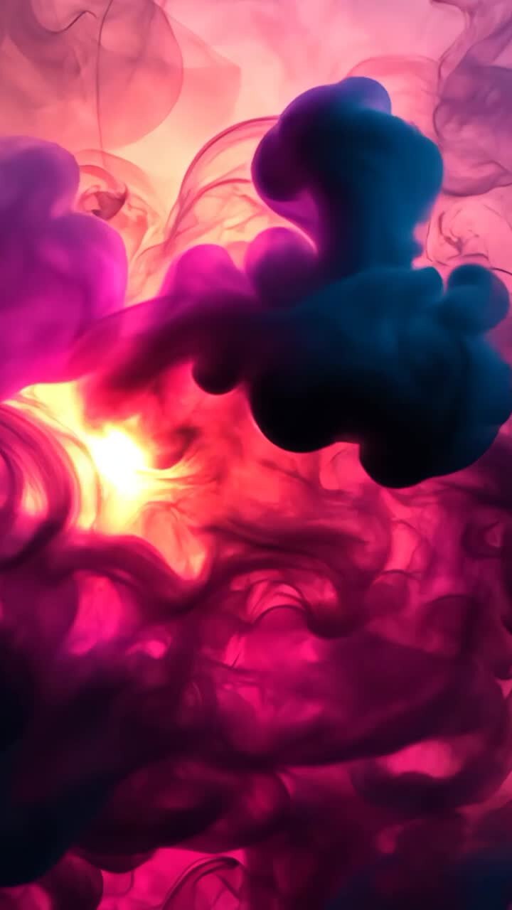 Vertical video: Warm backlight illuminating colored fluid plumes swirling in clear tank