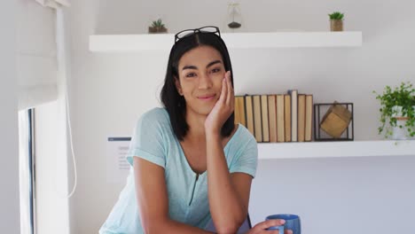 Portrait-of-mixed-race-gender-fluid-person-looking-at-camera-and-smiling-at-home