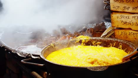 steaming hot cabbage stew being served from a large pan at a bustling food stall with smoke rising