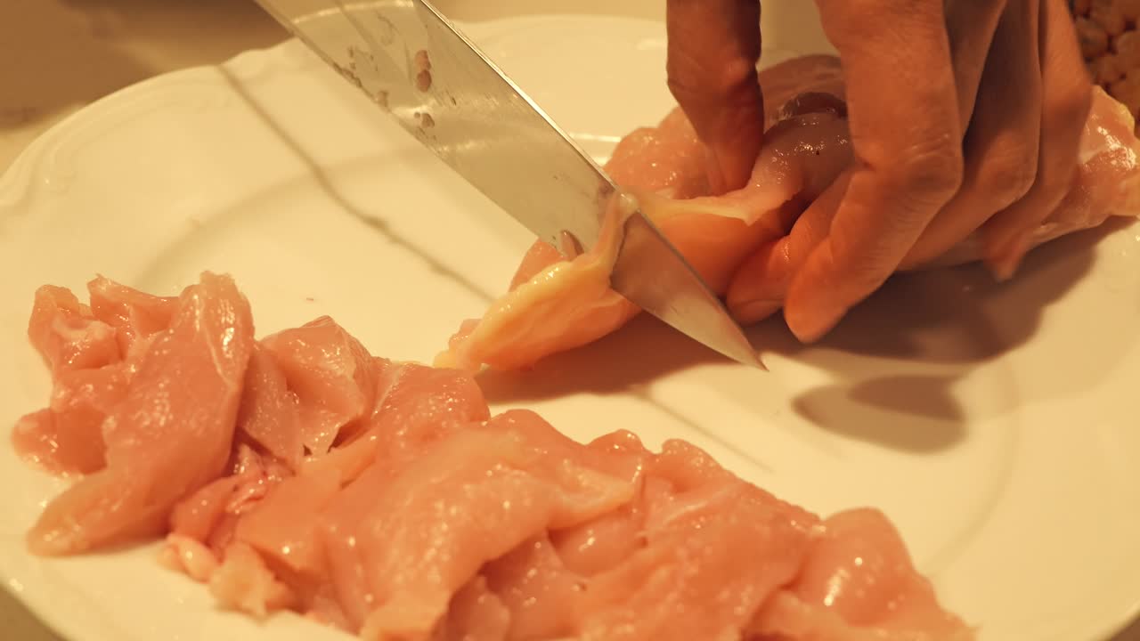 Close up of hands cutting raw chicken into thin slices on white plate