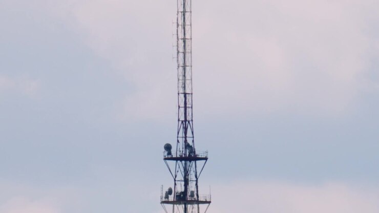 Una alta torre metallica di telecomunicazioni si erge contro un cielo pallido. Diverse antenne ed elementi strutturali sono visibili lungo la struttura verticale.