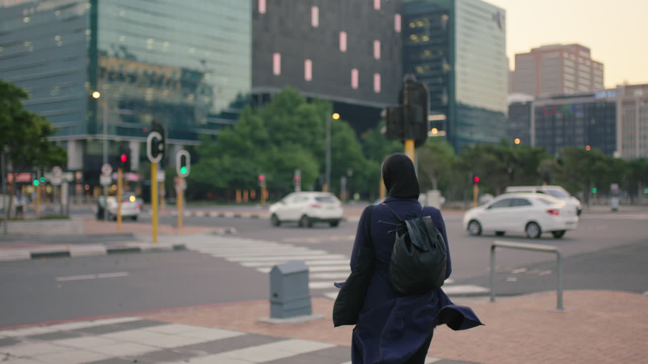 젊은 무슬림 사업가 인턴이 도시 거리에서 서서 바쁜 저녁 교통을 기다리고 하지브 헤드 스카프를 입고 있습니다.