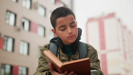 close up of student flipping through pages of novel while standing outdoors with blurred city building in background, showing focus on reading, curiosity for knowledge