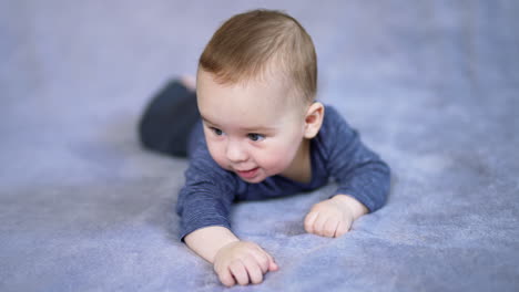 nice caucasian baby boy lying on his tummy on big bed. mom's hand reaches the son and he responds with a cute smile. grey backdrop in blur.
