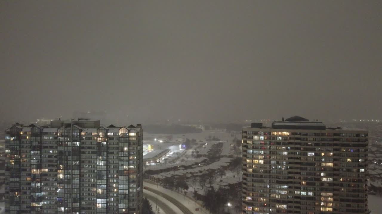 Aerial: evening cityscape with skyscrapers, lights and snow in Mississauga, Ontario, Canada, establishing drone shot