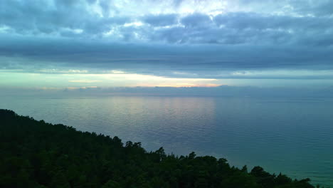 the scene unveils an awe-inspiring aerial perspective showcasing a tranquil body of water set amidst lush greenery under a magnificent sky embellished with billowing clouds