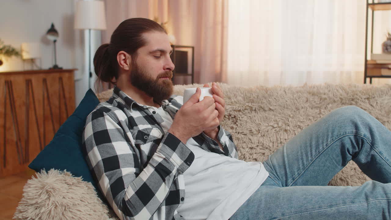 Young man lying with coffee mug at home sofa calm quiet break easy smile stressfree peace vibe