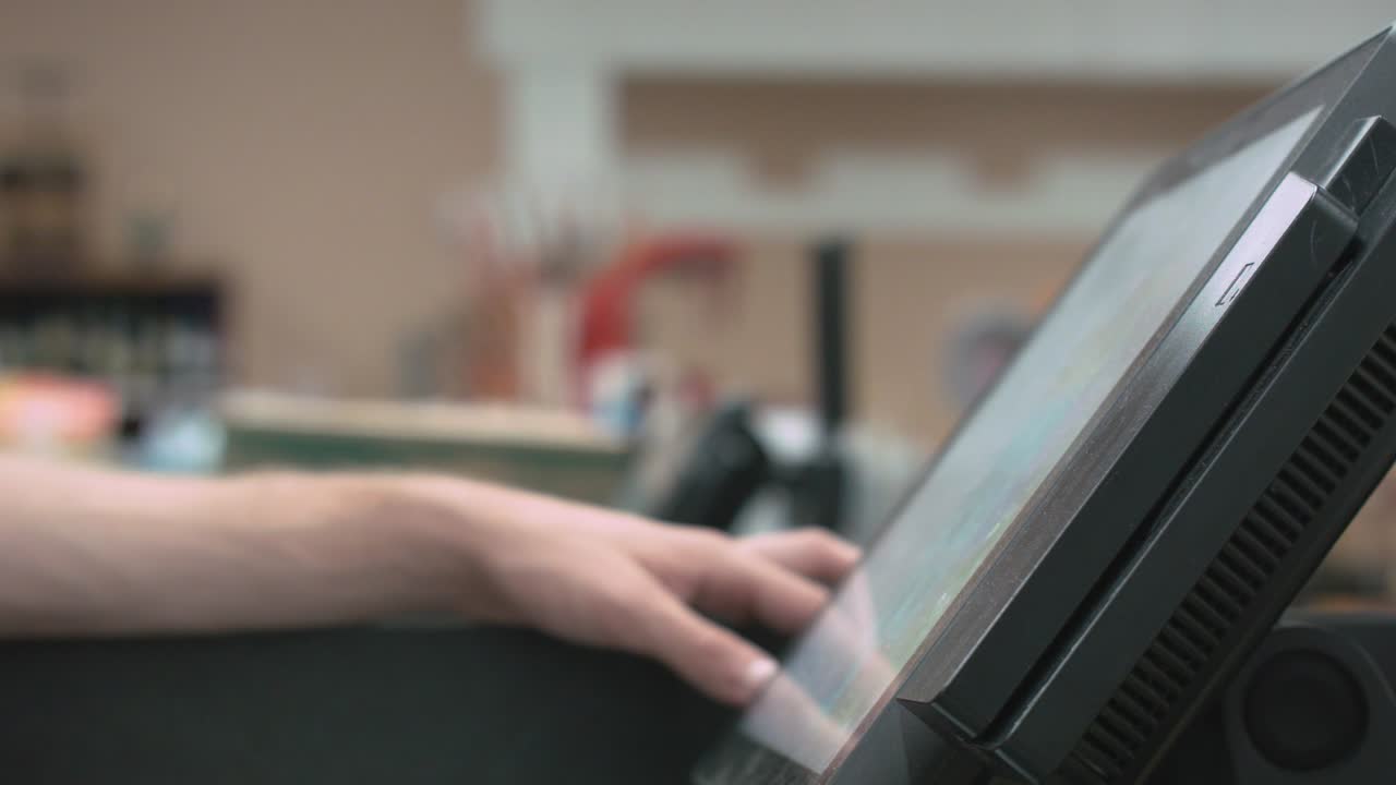 A profile shot of hands typing and making selections at a POS (Point Of Sale) system at a grocery store, shot under fluorescent lights. No distinguished branding.