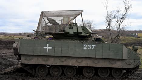 a mud-caked m2 bradley fighting vehicle on the ukrainian front. its medical marking and anti-drone cage armor are stark symbols of the realities of this modern war