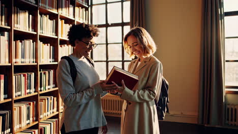 two students talking and sharing books in a library