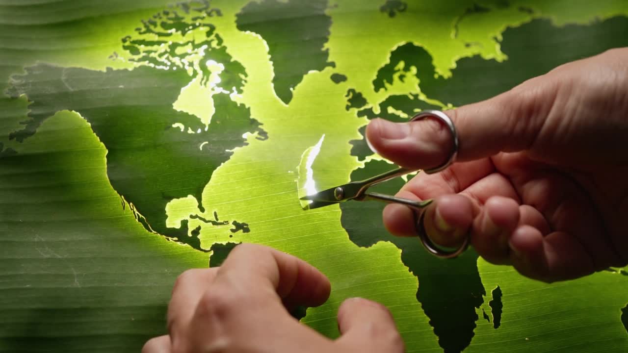 Mani che tagliano con mini forbici, la mano destra che entra stringendo una striscia sottile su una mappa appoggiata su un tavolo, creando una brace.