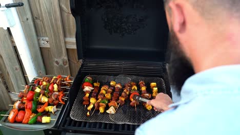 Caucasian-male-turning-chicken,-beef,-veggie-shish-kabob-skewers-on-grill,-over-shoulder-view