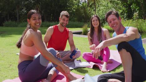 retrato de un instructor de yoga masculino sonriente y un grupo diverso feliz sentado en esteras en un parque soleado