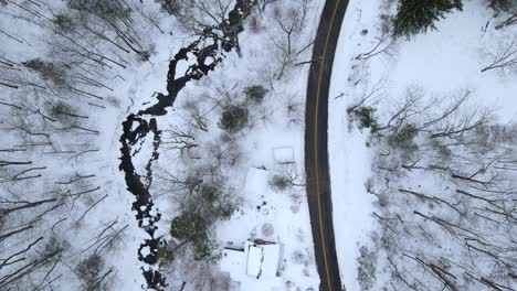 birds-eye view of a snowy, remote mountain road with a stream and forest