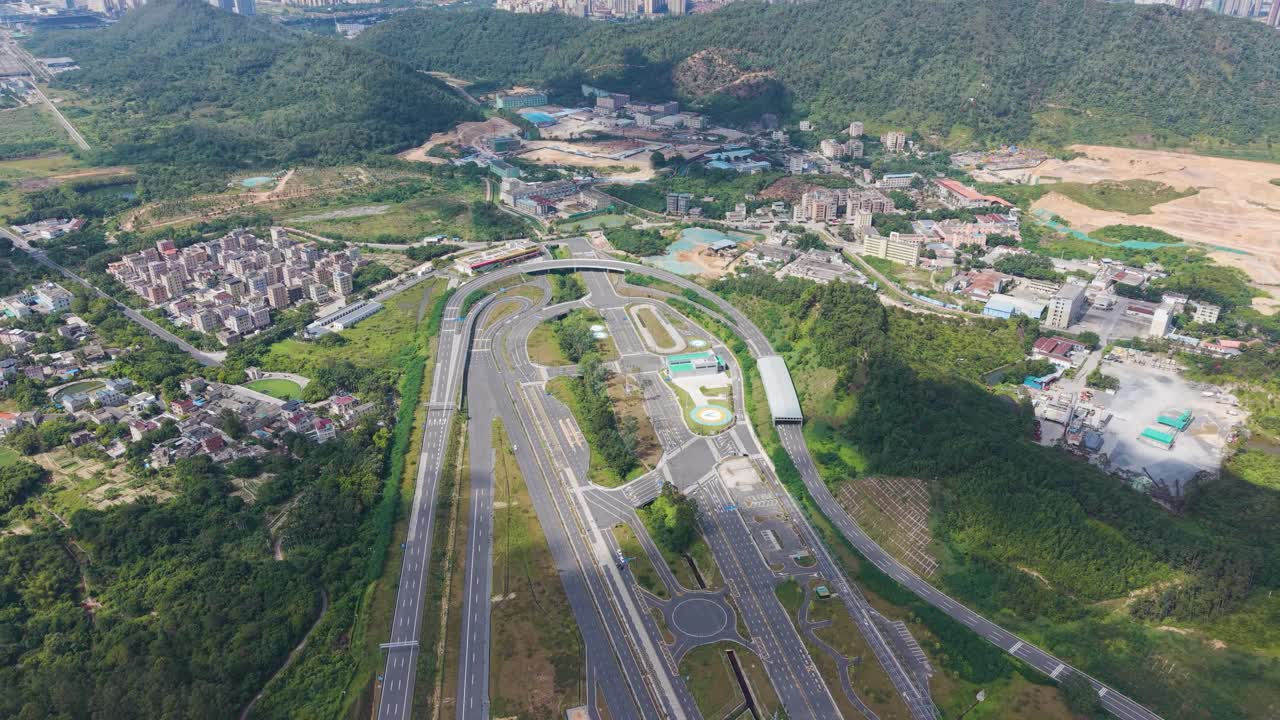 Expansive drone shot of Shenzhen’s large vehicle testing facility with multiple road surfaces, lanes, and testing zones surrounded by green hills and urban areas. Automotive and infrastructure themes