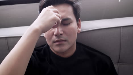 young man slouched on the sofa, feeling stressed and overwhelmed with a headache due to work exhaustion, societal pressure, and the impact of insufficient rest on mental health.