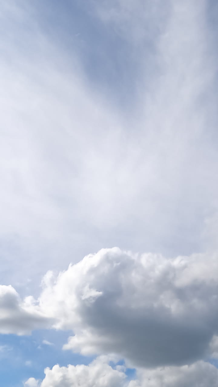 Cumulus and spindrift clouds transformation in the summer sky. Low angle view on the blue skies with multiple clouds. Timelapse. Vertical video