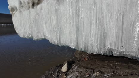 Gran-Formación-De-Hielo-Capturada-Bajo-El-Brillante-Sol-De-La-Tarde-De-Invierno-En-La-Orilla-De-Un-Río-En-Rusia,-Con-Agua-Clara-Y-Suelo-Fangoso-Visible