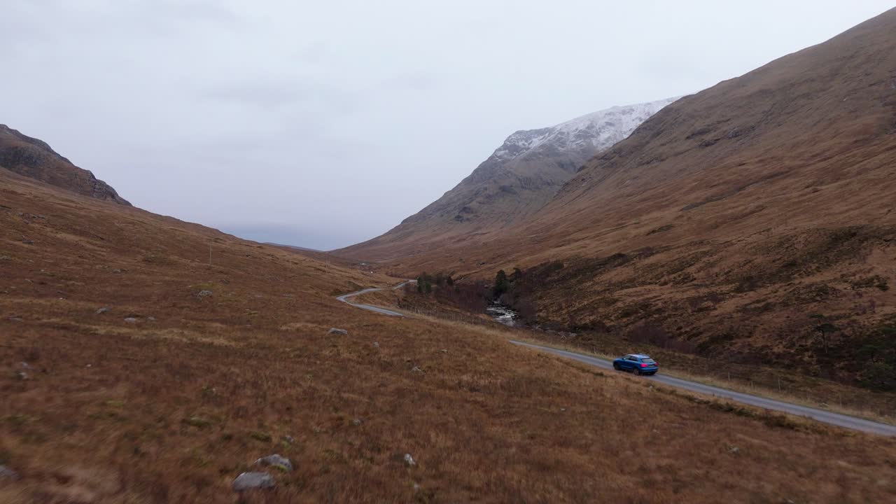 Car driving through Highlands moors, Glen Etive in Scotland, aerial tracking shot