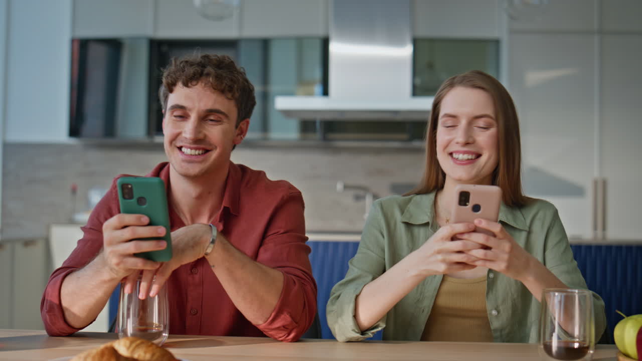 Young pair focused cellphones sitting kitchen closeup. Family couple looking
