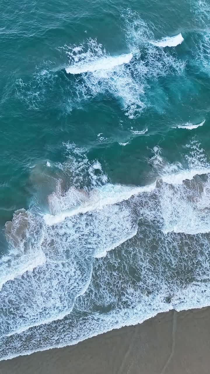 el dron captura las olas que se estrellan en la orilla arenosa.