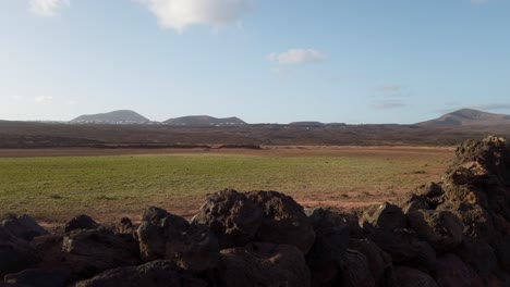 verdant plain bordered by rugged volcanic rocks with majestic mountain silhouettes under expansive sky in lanzarote's serene volcanic landscape, canary islands, spain