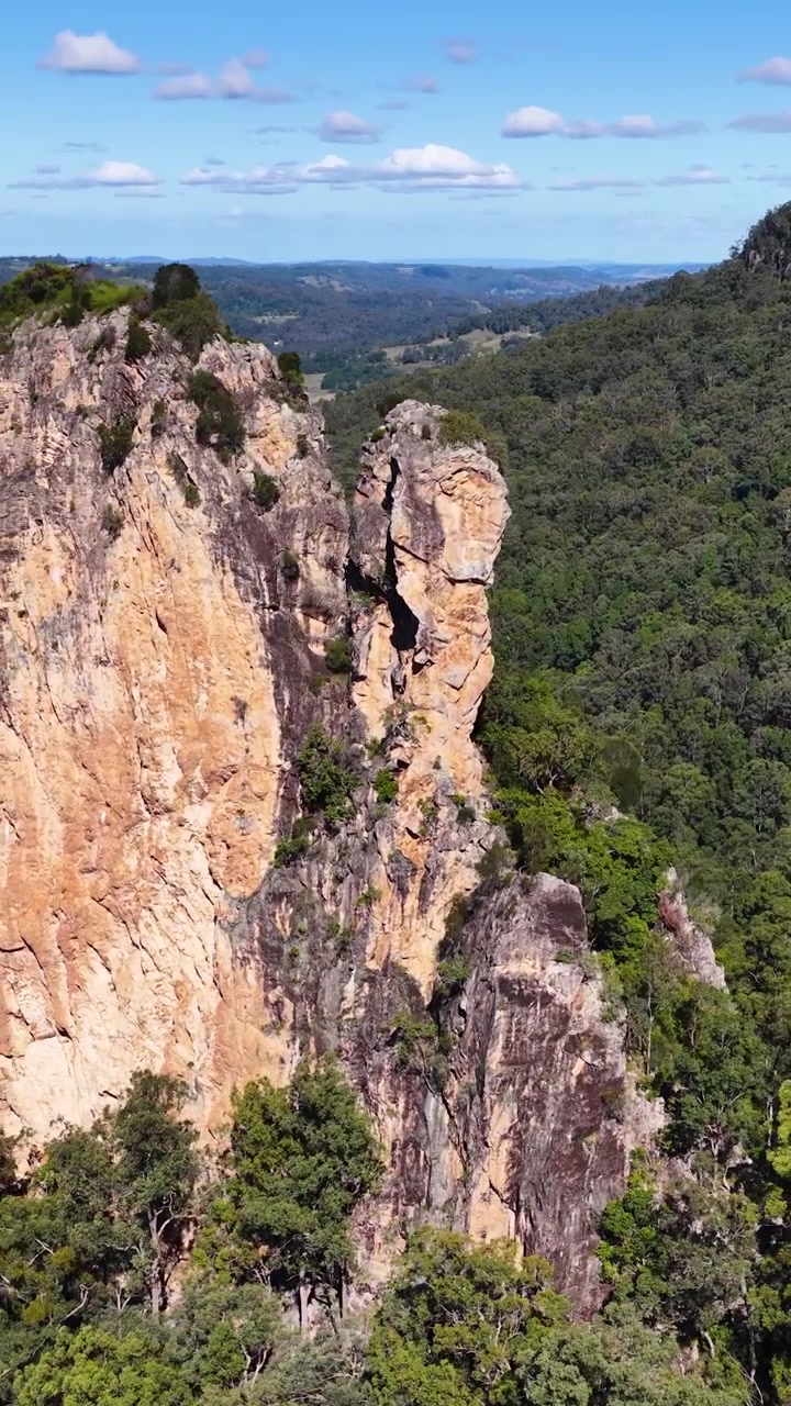 Un filmato di droni cattura la bellezza aspra delle Nimbin Rocks, mostrando scogliere imponenti e una vegetazione lussureggiante sotto cieli sereni.