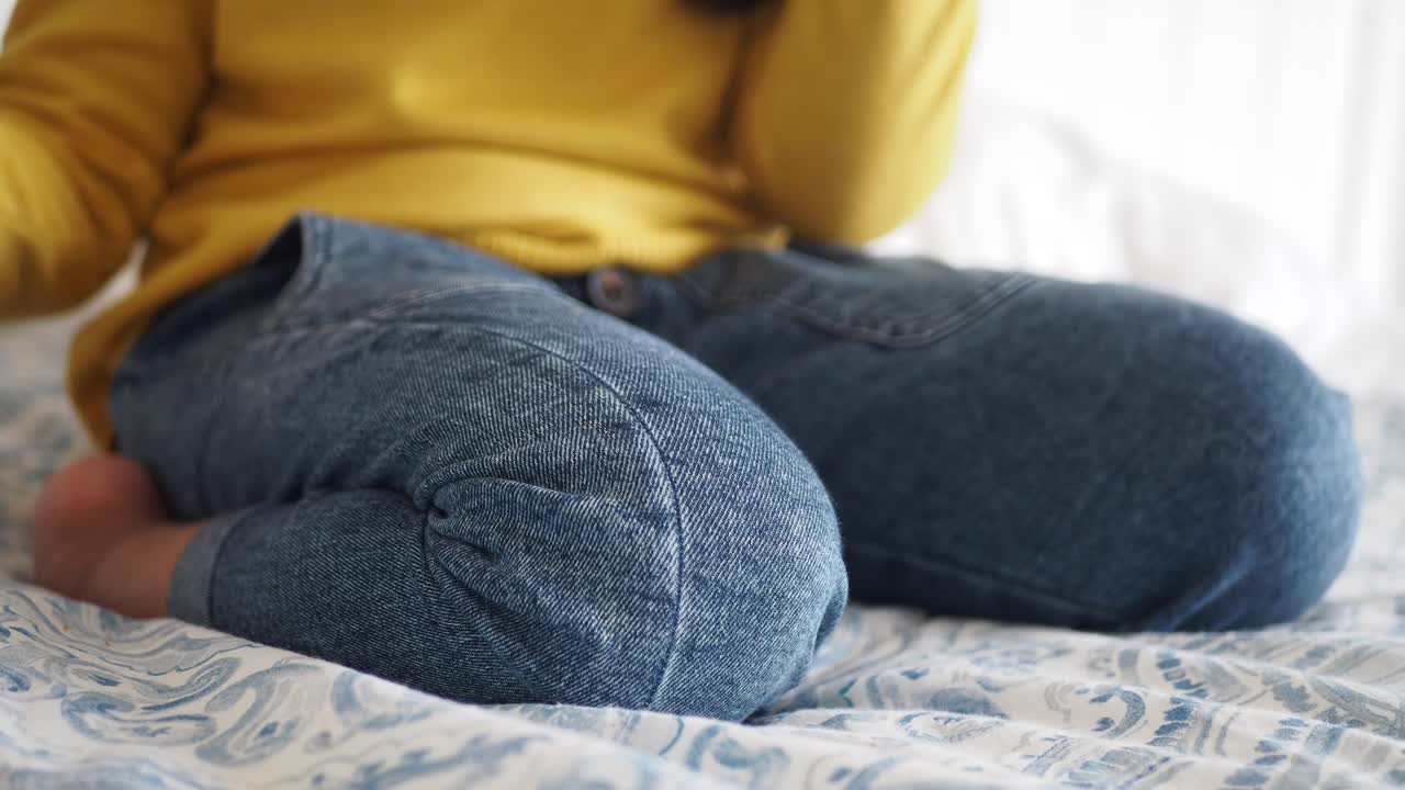 Person in blue jeans and a yellow sweater sitting on a bed