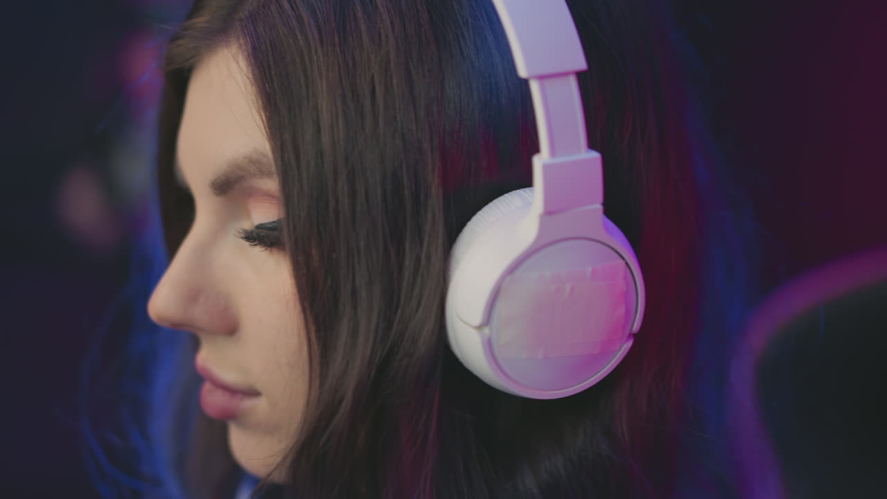 Close up gamer gently placing headphones over head while seated in subtle colorful room, surrounded by ambient pink and blue lighting, suggesting gaming setup