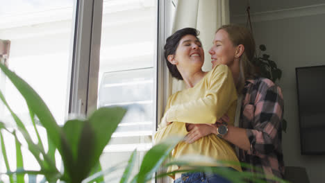 caucasian lesbian couple embracing each other near the window at home