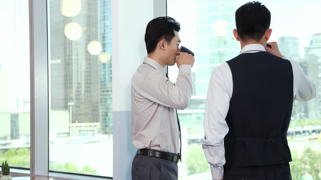 窓越しにオフィスビルの前に立つ2人のビジネスマンがコーヒーを飲んでいます。休憩中に同僚たちがビジネスプロジェクトについて話し合っています。チームワーク、交流、取引、協力のコンセプトです。