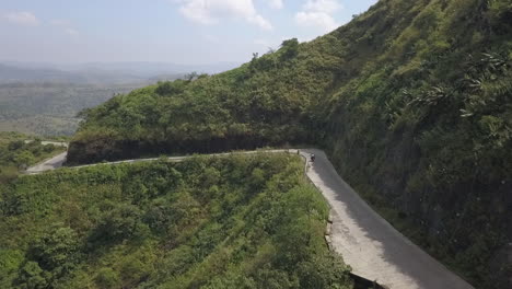 aerial follows motorcycle on twisty road cut into steep mountain side