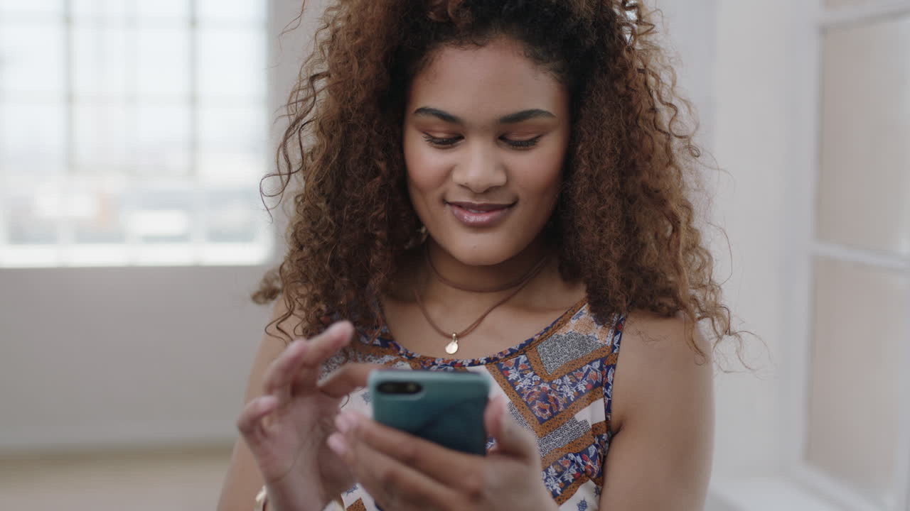 ritratto di una graziosa ragazza di razza mista che scrive messaggi di testo navigando sui social media usando lo smartphone godendo della comunicazione digitale online