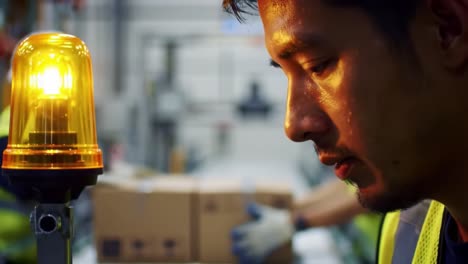Focused Worker Observing Alert Light in Warehouse Environment During Busy Operations, Highlighting Workplace Safety and Attention to Detail