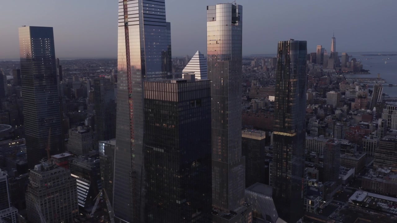 Grattacieli di vetro di Hudson Yards svettano sopra i densi isolati di Manhattan al tramonto, ripresa aerea a media altezza di riflessi di luce scintillanti, panoramica di New York di un complesso privato