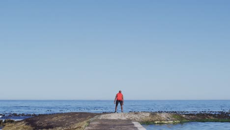 hombre afroamericano senior ejercitando levantando las manos junto al mar