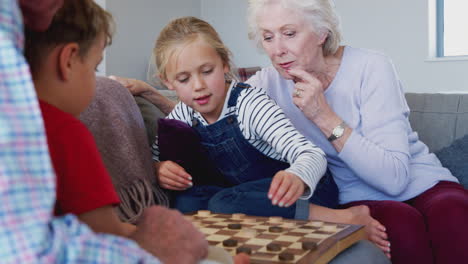 grandparents playing board game of draughts with grandchildren at home