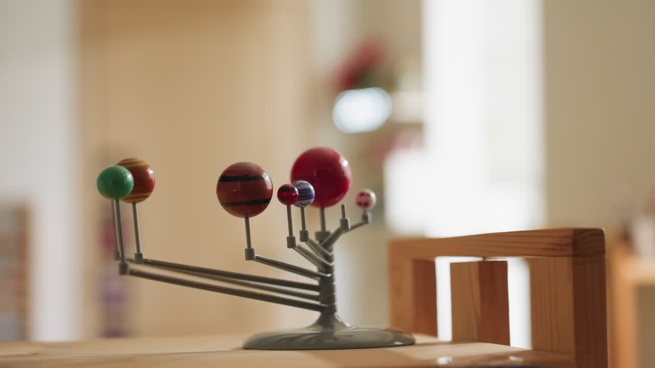 Close up of colorful planet model representing solar system placed on wooden table inside bright classroom. Soft bokeh background creates warm educational atmosphere