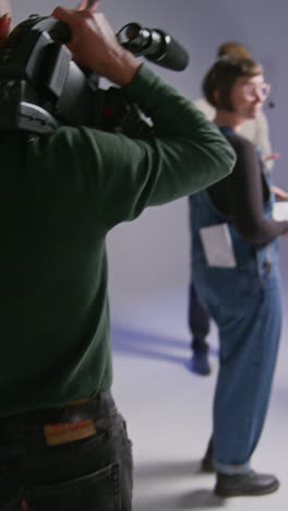 vertical video of film cameraman shooting movie handheld on busy film set in studio with sound recordist and assistant