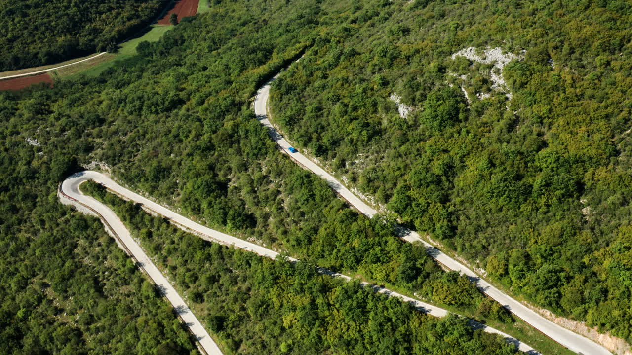 vista aérea de un coche azul conduciendo por una sinuosa carretera de montaña en istria, croacia