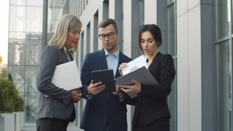 businessman and female colleagues with documents and tablet device, talking and discussing about a project in the street