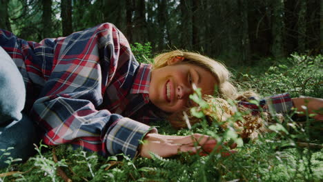 Girl-lying-on-green-grass-in-forest.-Cheerful-woman-touching-fern-leaves