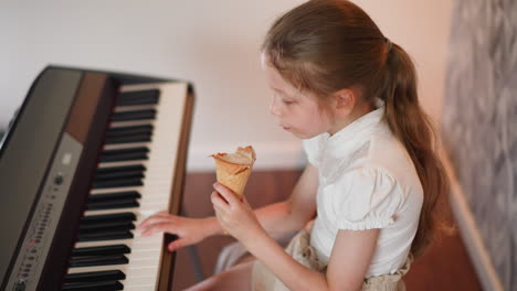 overhead view of young girl holding ice cream cone while gently pressing piano keys, showing blend of leisure and learning in relaxed indoor setting