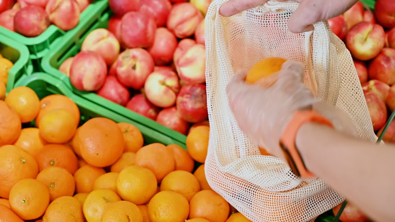 Man's hands putting tangerines in a reusable ecological bag in the supermarket. Ecology idea